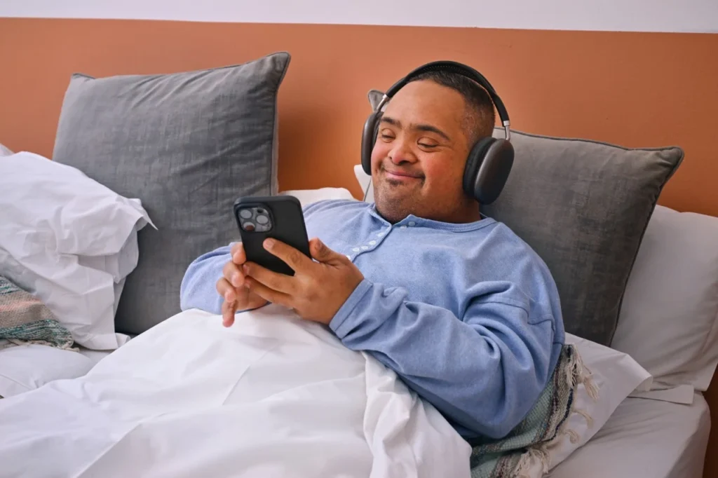 Disabled man with down syndrome in bed looking at phone and smiling